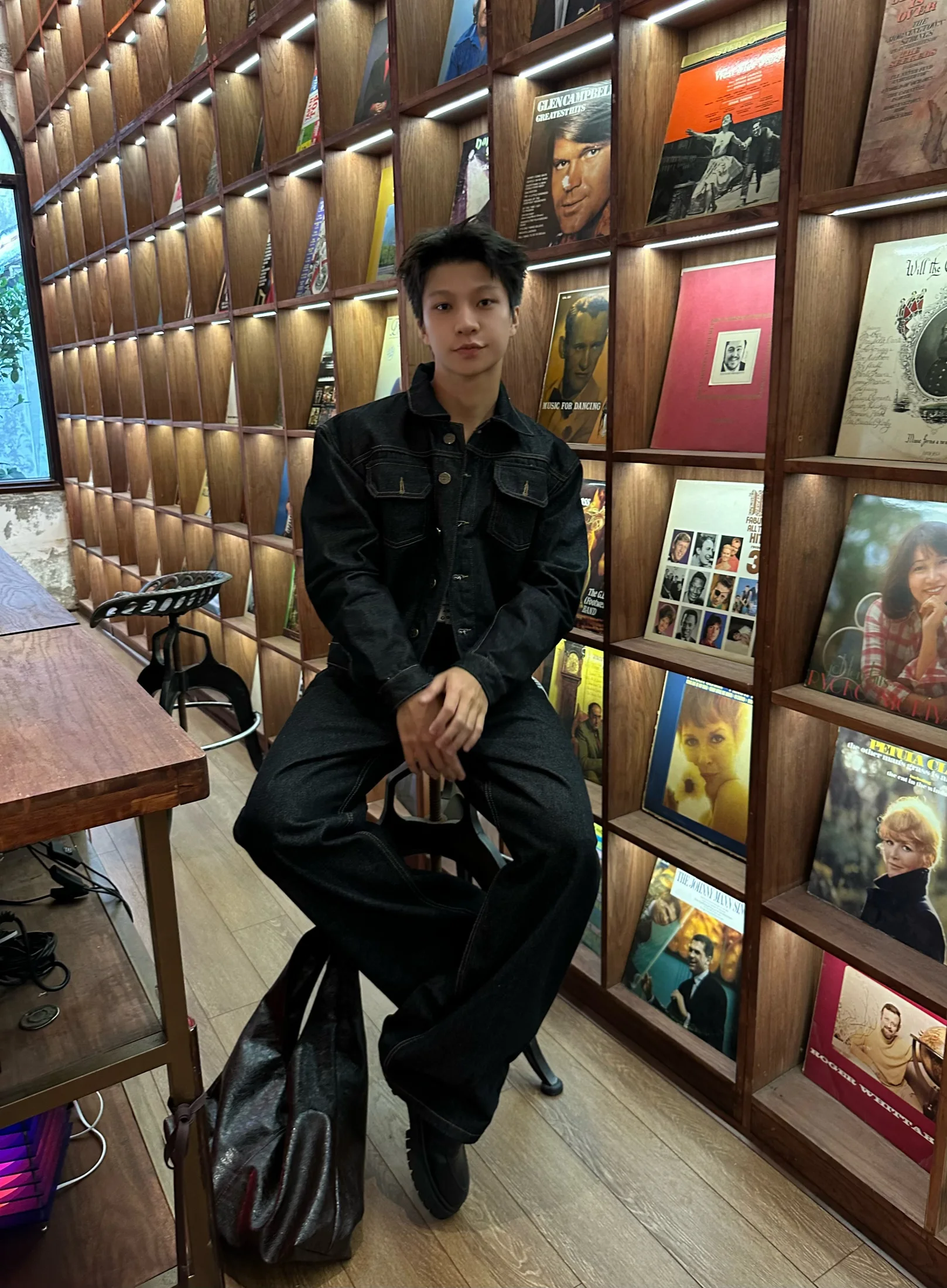 Nguyễn Khánh Hưng seated in a dark denim outfit by a wall of records