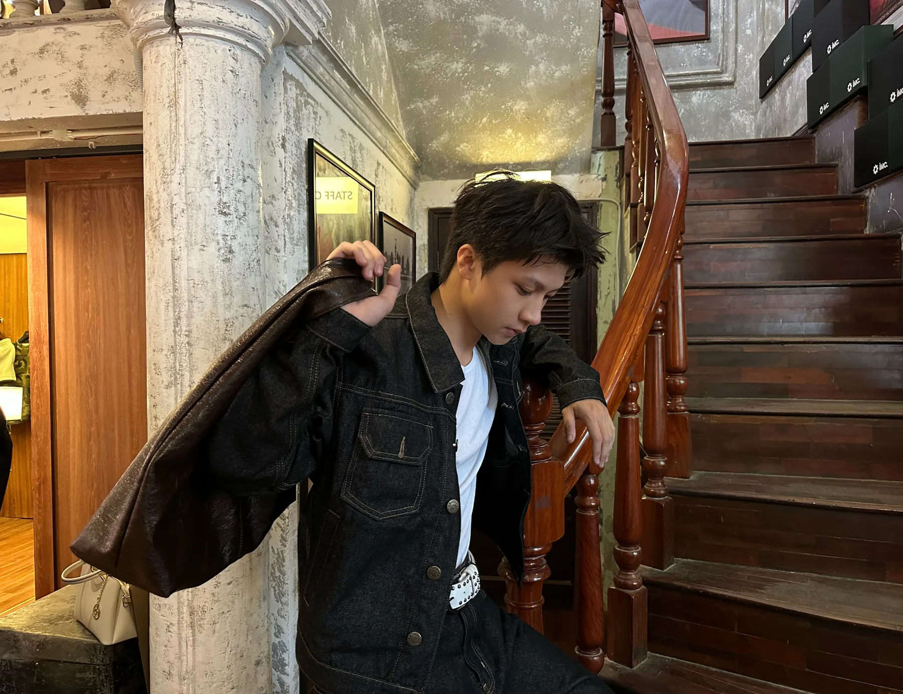 Nguyễn Khánh Hưng carrying an oversized leather bag beside a wooden staircase